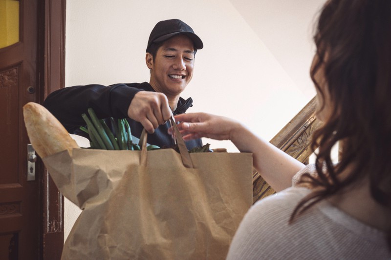 Ein junger Mann überreicht einer Frau an der Haustür eine Tüte mit Lebensmitteln.