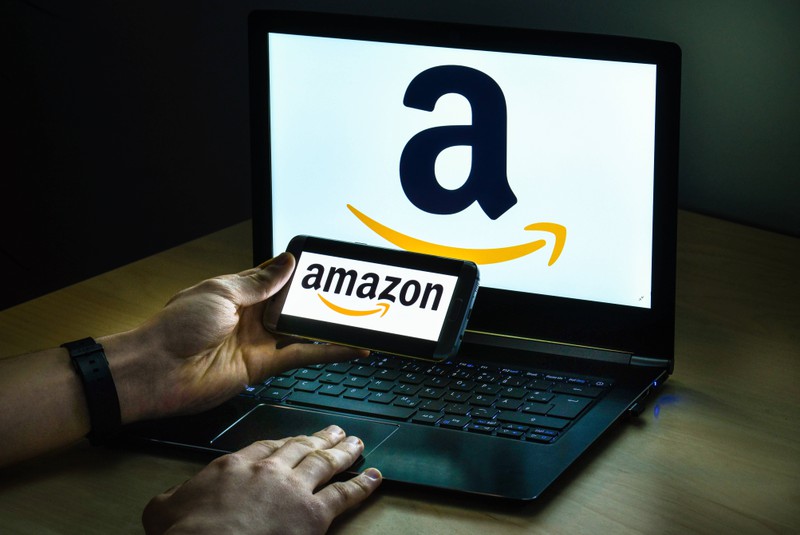 Ein Mann sitzt vor einem Laptop und einem Smartphone, auf denen das Amazon-Logo zu sehen ist.