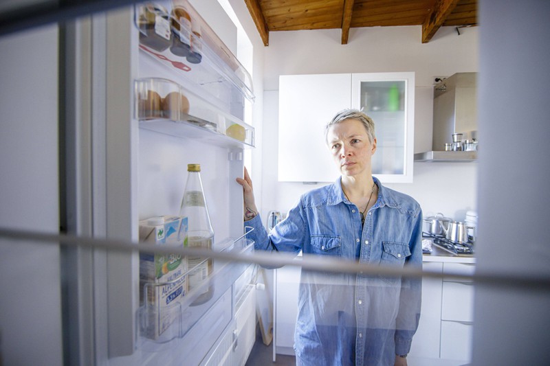 Zu sehen ist eine Frau, die gerade einen Kühlschrank öffnet.