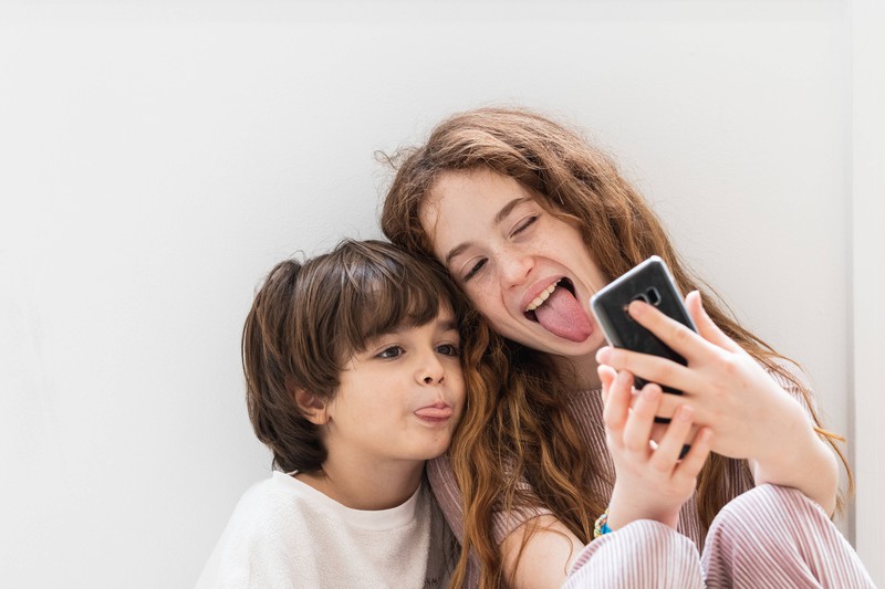 Zwei Kinder sitzen nebeneinander und schneiden Grimassen für ein Selfie
