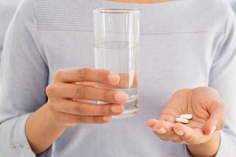 Frau hält Tabletten und ein Glas Wasser in den Händen