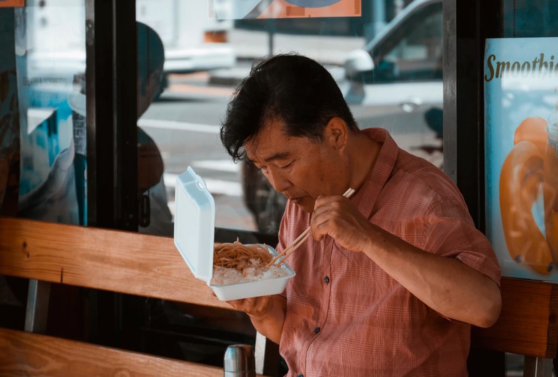 Asiatischer Mann isst Reis und Nudeln aus Plastikverpackung