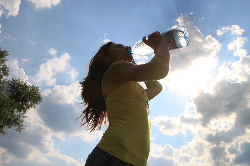 Man sieht eine Person, die aus einer Wasserflasche trinkt und die Wasserflasche sollte man niemals im Sommer im Auto lassen.