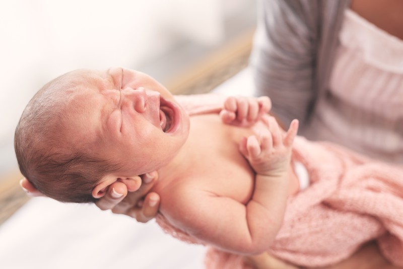 Säugling brüllt in den Händen seiner Mutter