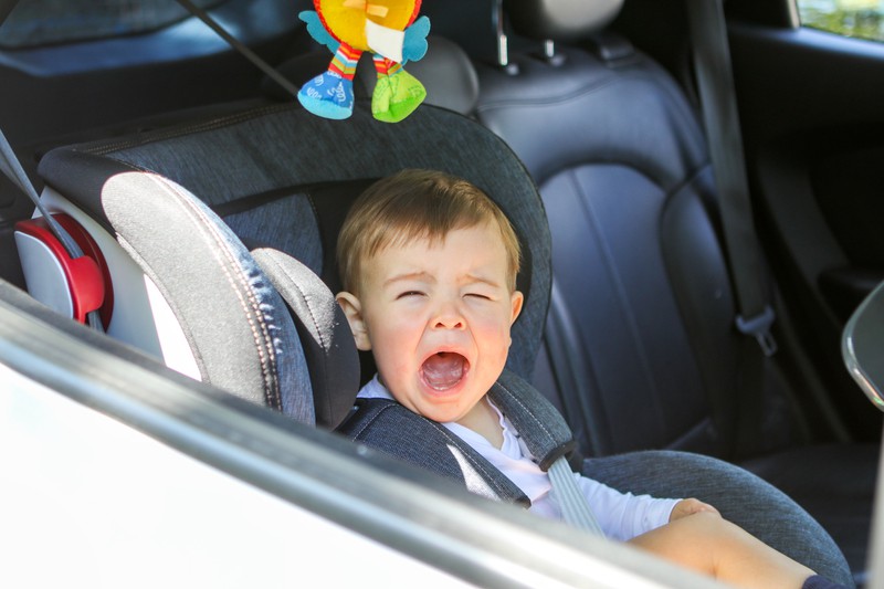Kleiner Junge liegt im Autositz und weint