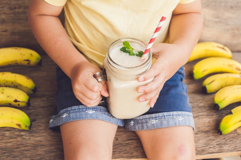 Kind hält Bananen-Smoothie in der Hand