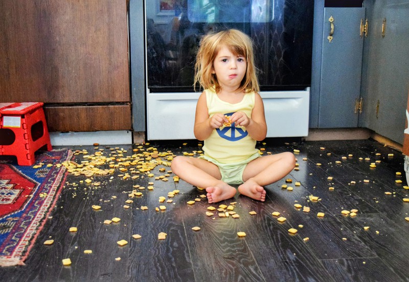 Kleinkind sitzt zwischen Cornflakes auf dem Boden