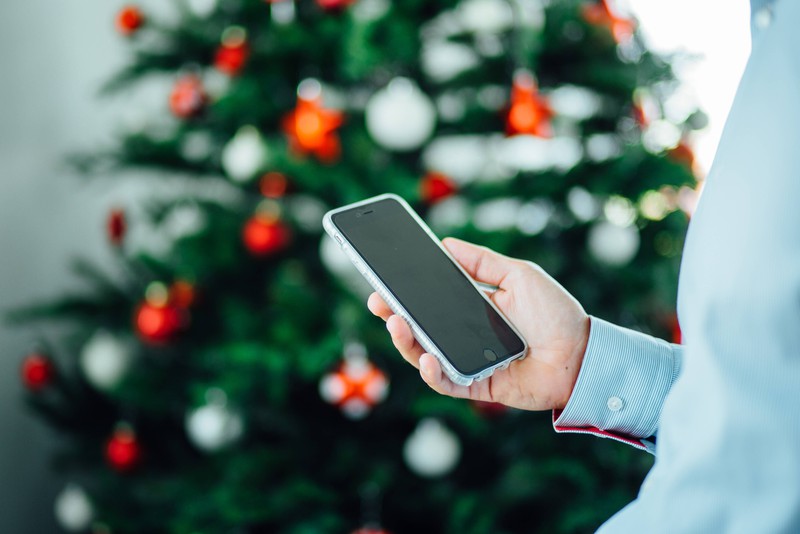 Man sieht ein Smartphone vor einem Weihnachtsbaum, das Elektrogerät ist das Weihnachtsgeschenk