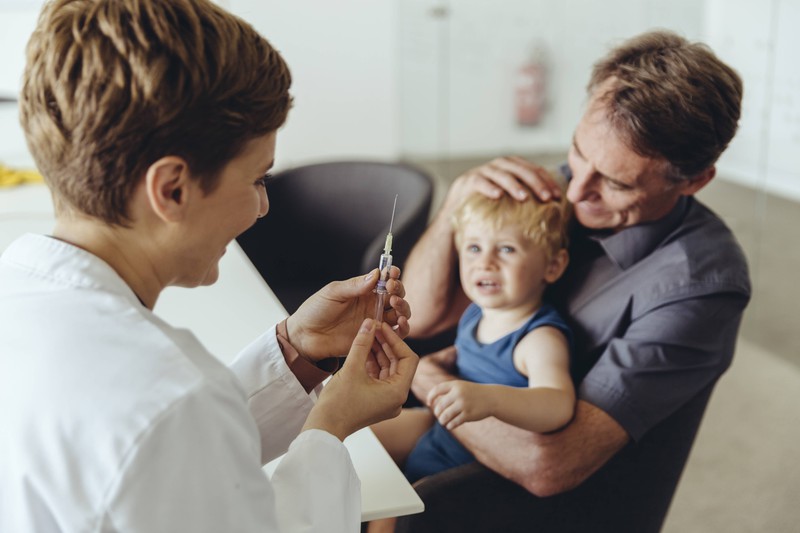 Ein Arzt mit Spritze, die einen Jungen impfen möchte, um eine Erkrankung zu vermeiden.