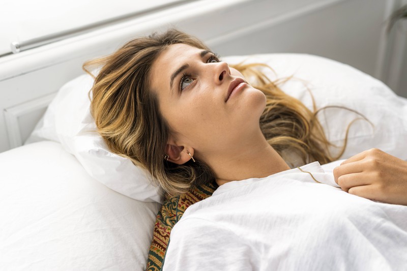 Eine Frau liegt wach im Bett, weil sie vom Zähneknirchen Kopfschmerzen hat
