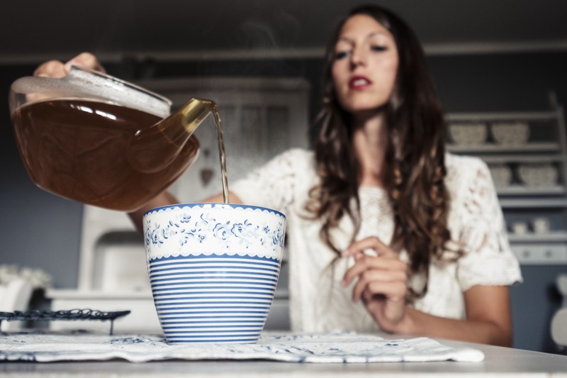 Eine Frau kocht heißen Tee auf und gießt ihn in eine Tasse
