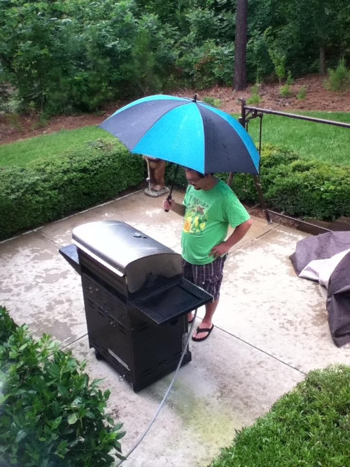 Man sieht einen Vater, der im Regen steht und trotzdem grillt
