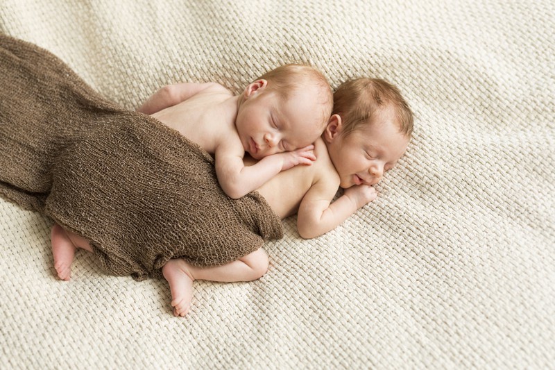 Zwillinge liegen aneinander gekuschelt unter einer warmen Decke und spenden sich Kraft