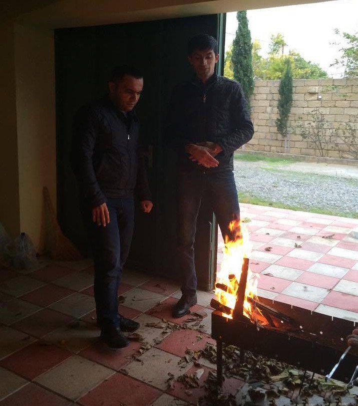 Zwei Männer stehen vor einem Feuer und es wirkt so, als würde das Bein eines Mannes brennen.