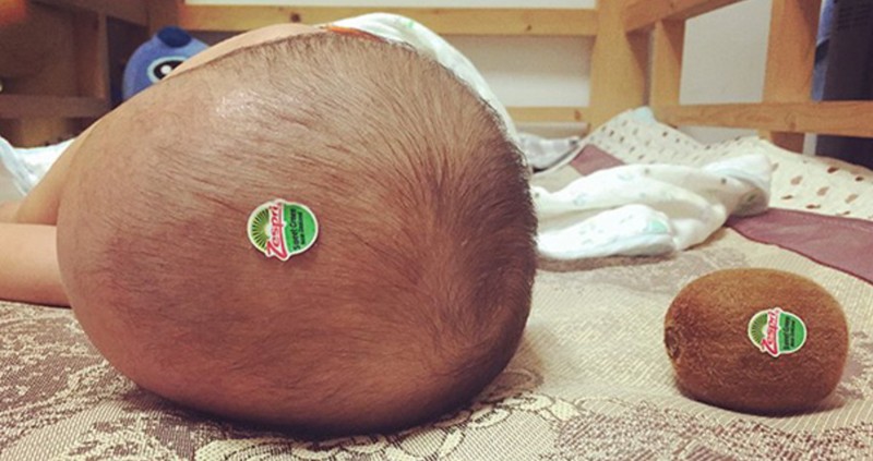 Ein Vater, den man alleine mit dem Baby gelassen hat und er einen Kiwi-Sticker auf seinen Kopf klebte