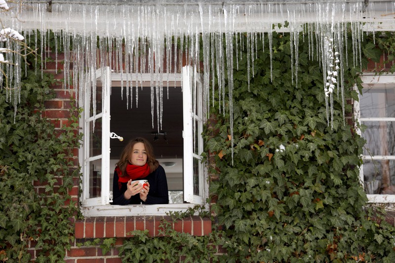 Eine Frau steht am offenen Fenster im Winter