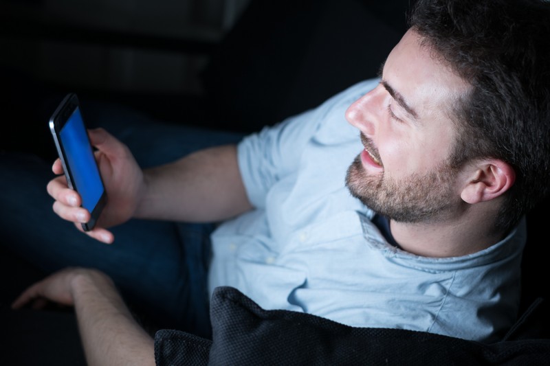 Der Mann schläft schlecht, weil er unterbewusst immer und immer wieder auf sein Handy achtet.