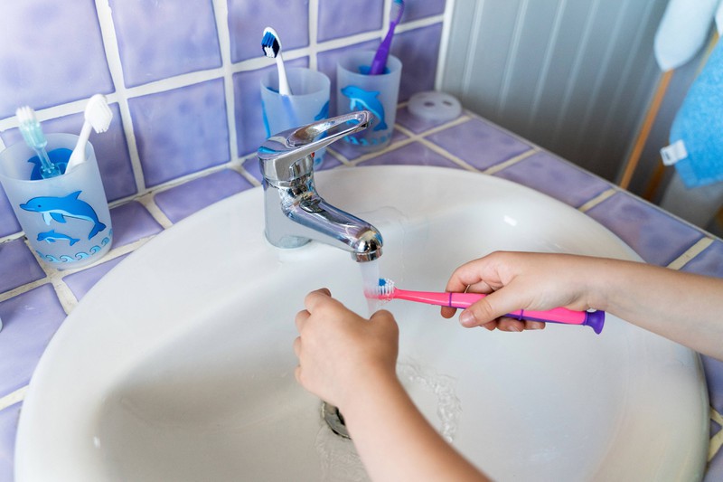 Ein Kind hält eine Zahnbürste unter das Wasser im Waschbecken