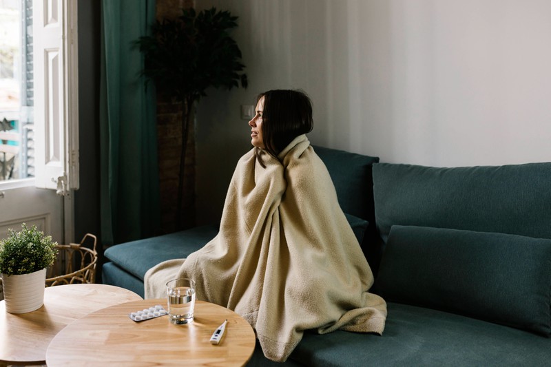 Eine Frau sitzt mit einer Decke auf dem Sofa und schaut aus dem Fenster